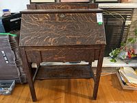 Front view of vintage wood secretary desk with drop-front panel closed and drawer below.