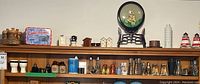 Wide shot of wooden shelf displaying various salt and pepper shakers, decorative tins, small figurines, and kitchen decor items including a dog plate, small house shakers, and blue and white shakers.