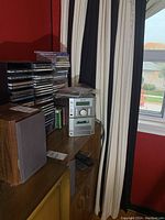 Photo of Sharp XL-570 stereo system, speakers, and stacked CDs on a wooden cabinet in a room with red walls and window.