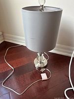 Side lamp with grey fabric shade and chrome base with crystal ball detail, viewed from the front on wooden floor.