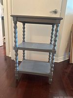 Side view of the grey side table showing two lower shelves and spiral turned legs.