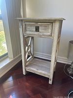 Front and side angle showing grey wooden side table with drawer and decorative side panels.