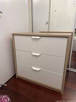 Front view highlighting 3 white drawer fronts with angular white handles and wood frame.