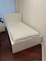 Full view of the IKEA twin bed with white bed frame, fitted mattress, and headboard against a wall.