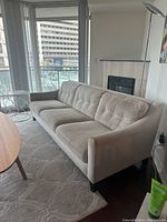 Light grey fabric 4-seater IKEA sofa in living room with tufted back cushions and brown wooden legs.