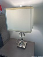 Full view of white and chrome side lamp with square shade on a surface.