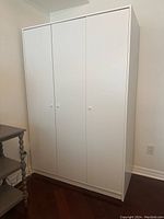 Front angle view of white 3-door IKEA cabinet closed showing clean white doors with three small white knobs