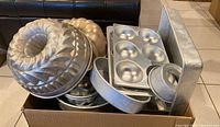Various metal Bundt pans, muffin pans, round cake pans stacked inside a box
