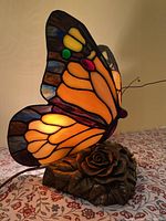 Side view of the butterfly lamp showing the stained glass wings and bronze rose base on a floral tablecloth.
