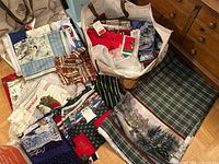Photo showing multiple folded and bundled Christmas-themed fabric pieces with various holiday prints and colors in bags and spread on floor.