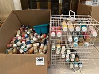 Box containing numerous assorted craft paint bottles, mostly partially used, in various colors and brands.