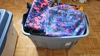 Photo showing a large gray bin filled with various folded vintage fabric pieces including floral and abstract prints in vibrant colors.