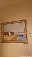 Framed oil or acrylic painting depicting coastal harbor scene with boats and buildings, signed by Laura Eastwood.