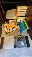 Overall image of office supplies including paper stacks, binders, woven basket with photo paper and cable ties