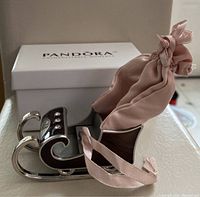 Metal Santa's sled ornament with pink fabric sack and crystals shown from front angle with Pandora branded box in background