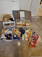 Photo showing several blank scrapbooks, a plastic drawer organizer containing various scrapbooking materials, multiple rubber stamps, and punch tools arranged on the floor.