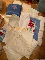 Photo showing a collection of folded tablecloths, napkins, towels including blue towel and floral printed white fabric