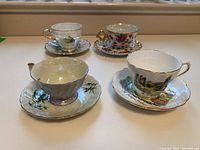 Overview of all four teacups and saucers arranged on a windowsill, showing varied designs and styles.