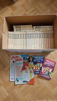 Photo showing all 34 Trixie Belden books arranged by volume number inside a cardboard box with 2 Jam magazines placed in front.