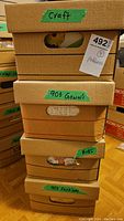 Stack of four labeled cardboard boxes containing sewing patterns and craft materials, each labeled with green tape as Craft, 90's Gowns, Kids, and 90's Fashion.