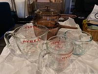 Four Pyrex measuring cups of various sizes, clear glass with red measurement print, some print fading visible.