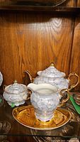 Full set showing teapot, creamer, sugar bowl, and plate with porcelain pieces featuring light blue marbled design with gold trim against wooden background.