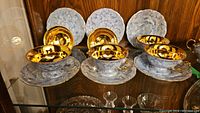 Wide view showing six porcelain teacups with gold interiors and six matching blue and white saucers with gold trim.
