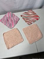 Four handmade knit washcloths placed on a flat surface showing two variegated colored squares and two solid beige squares.