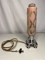 Full view of antique pink torpedo glass lamp with plugged cord and chrome scroll base on white surface.