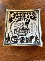 Square white porcelain change tray with black graphic Betty’s Bathtub Gin design on top surface.