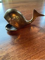 Side view of brass whale ashtray showing rounded body and open mouth ash holder