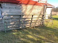 Full gate leaning against concrete barn wall on grass field, view of entire length.