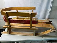 Side view of Mastercraft wooden child's sled showing bench seating, red painted backrest and side rails, and metal runners.