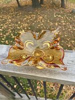 Amber art glass ashtray or bowl photographed outdoors on a wooden railing, clear view of ruffled edges and base shape
