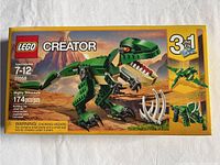 Front of box showing Lego Creator Mighty Dinosaurs set 31058 with 174 pieces, suitable for ages 7-12, featuring a green dinosaur T-Rex model in a volcanic landscape.