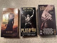 Front view of three factory sealed VHS tapes: Gladiator, Platoon, Schindler's List