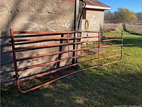 Red farm gate leaned against a wall, showing horizontal bars and the bent shape spanning 165 inches in length.