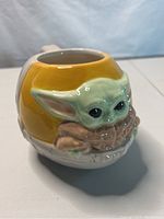 Front view of ceramic sculpted Baby Yoda mug showing detailed sculpted face and ears with bowl held by the character.