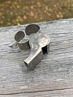 Top and side view of the silver-toned metal whistle with metal clip, showing the shape and clip detail.