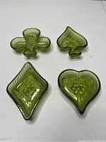 Four green glass dishes, shaped as club, spade, diamond, and heart, arranged on flat surface.