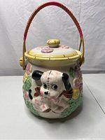 Front view showing white dog in 3D on cookie jar with colorful flowers and woven bamboo handle.