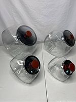 Four vintage clear glass candy jars with slant design, metal lids and wooden knobs arranged on white surface.