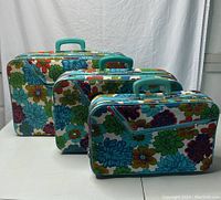 Front and side view of three vintage suitcases in different sizes with colorful floral patterns and turquoise handles.