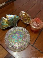 Photo of four art glass pieces arranged on a wooden table showing a large leaf plate, a round plate with the partridge and pear design, a lidded dish, and a small sunflower dish.