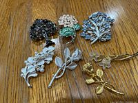 Seven floral brooches arranged on wooden surface showing variety of metallic and gemstone-style details.