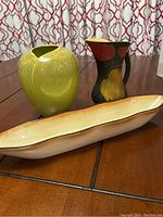 Photo showing the three items in the lot: green vase, black floral pitcher, beige olive dish.