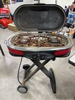 Front view of Coleman Roadtrip portable propane grill with lid open, showing two propane burners and grilling surface inside the lid.