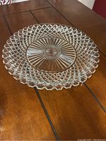 Clear round crystal platter with trellis lattice edge and sunburst pattern center on wood table