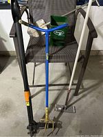Full set of five garden tools including seed spreader, weed puller, aerator, shovel, and sanding block with handles, displayed on a chair in garage.