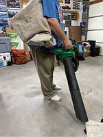 Photo of person holding the assembled leaf blower with cloth collection bag attached to backpack straps.